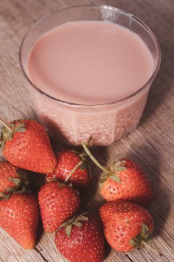 Çilek aromalı süt, ahşap zeminde berrak bardakta.