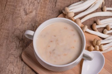 Ahşap zeminde beyaz bir fincanda mantar kremalı çorba.
