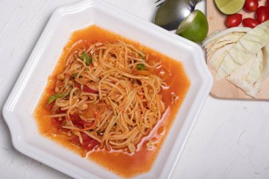 Beyaz tabakta Tayland papaya salatası. Beyaz arka planda popüler yemekler.