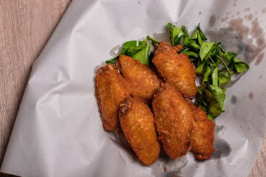 Ahşap zeminde beyaz tabakta kızarmış tavuk kanadı.