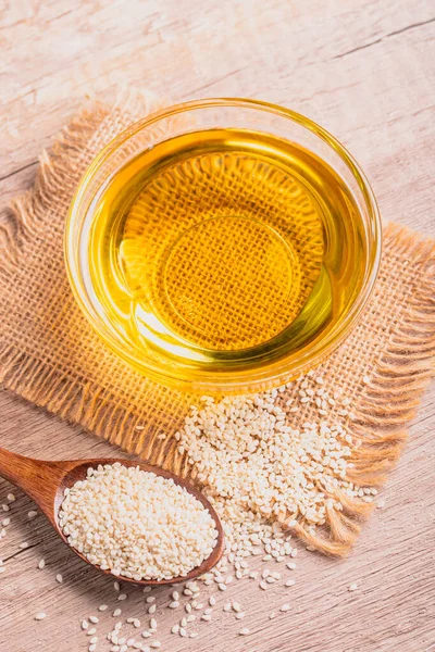 sesame oil in a bowl and white sesame seeds on wooden background