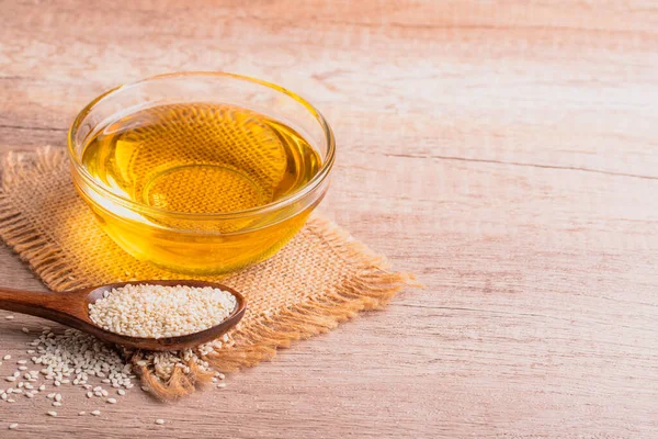 sesame oil in a bowl and white sesame seeds on wooden background