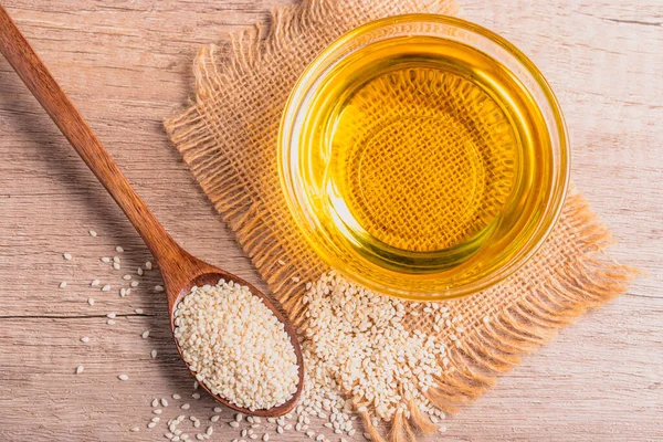 sesame oil in a bowl and white sesame seeds on wooden background