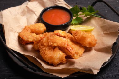 Breaded and breaded shrimp with chilli sauce on black background