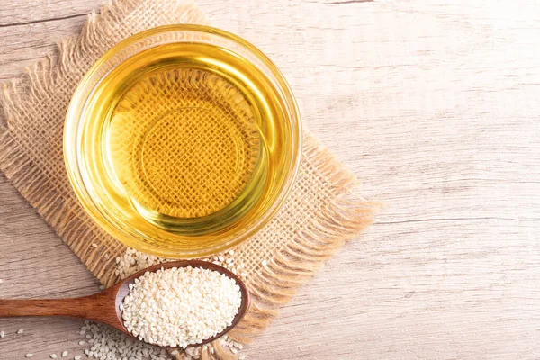 sesame oil in a bowl and white sesame seeds on wooden background