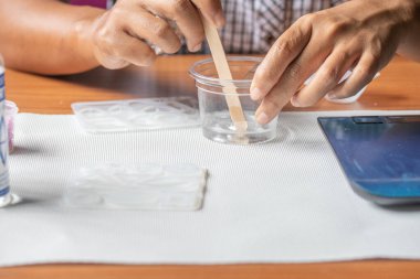 Hand mixing resin in plastic glass for jewelry making.