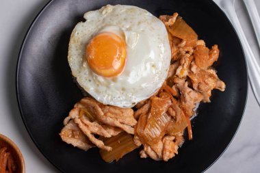 Kızarmış domuz eti, turşu ve siyah tabakta sahanda yumurta. Kore yemeği..