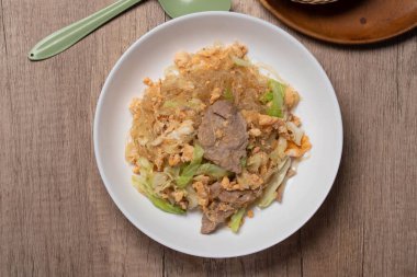 Stir fried vermicelli with pork, egg and collard greens in a white plate.