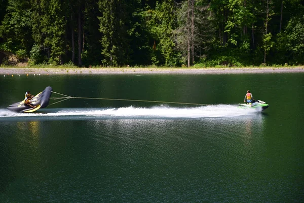 A jet ski pulls an inflatable sports raft with two men and entertains them — Stock Photo, Image