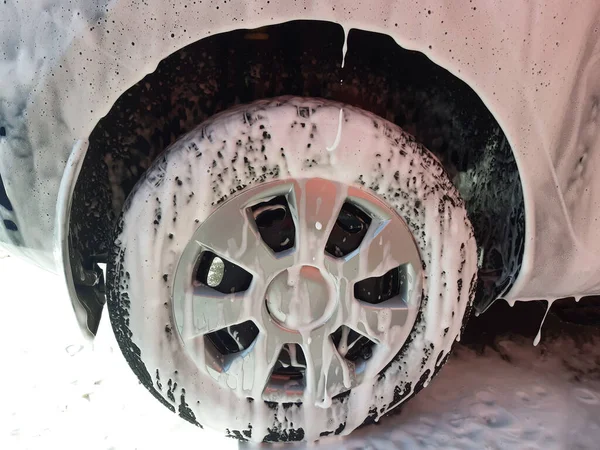 Arabanın tekerleği ve arabanın çamurluğunun bir kısmı tamamen araba yıkamada suyla yıkanmak için hazırlanmış beyaz köpükle kaplanmış. Köpük asfalta akıyor.