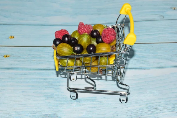 Framboesas, groselhas e groselhas são empilhadas em um carrinho de compras de brinquedo pequeno. close-up fotografado — Fotografia de Stock