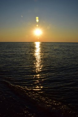Sabah güneşi, sakin dalgalarda yansıyan kumlu kumsalın arka planına vuruyor.