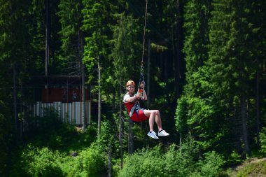 Miğferli genç bir adam bungee jumping 'den atladı ve şimdi bir ipe tutunuyor, yeşil bir ormanın bulanık arka planına karşı kendini bir spor kamerasında sallıyor ve filme çekiyor.