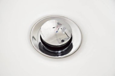 Banyo lavabosundaki su giderinden parlak bir tıkaç. Diş fırçası ve diş macununu yansıtıyor. Ve beyaz seramik lavaboların etrafında