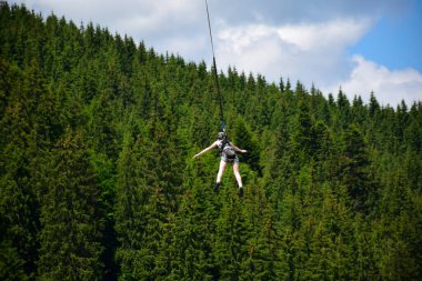 Kız bungee jumping gezisinden atladı, yüksek irtifada sıkı bir ipe tutundu. Bir dağ yamacının bulanık arka planında