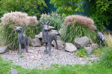Taşlardan bir tepede geyik figürleri ve parkı süslemek için uzun otlar.
