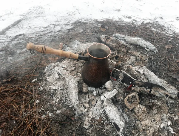 Un cezve de cobre con café se cocina en las brasas calientes de un fuego, y hay nieve alrededor de él. —  Fotos de Stock