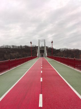 Köprü üzerinde asfalt kırmızı renkli yol perspektif olarak bölünmüş. Yan taraflarda lambalar var.