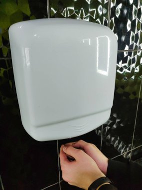 Hava otomatik el kurutma makinesi duvarda asılı ve çocukların elleri altında kurumuş.