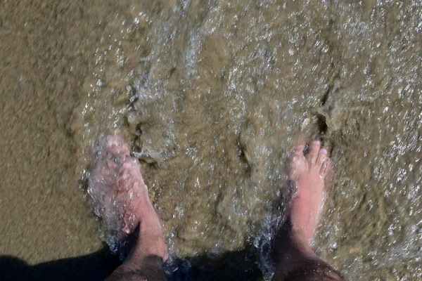 Dois pés de uma pessoa inundada por uma onda costeira, imersa na areia — Fotografia de Stock