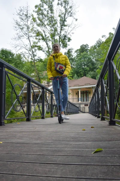 一位年轻女子骑摩托车在公园里有栏杆的桥上 从较低的角度来看 — 图库照片