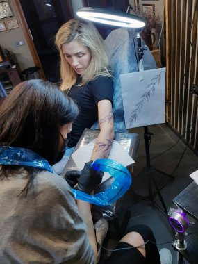 Dövme salonunda koluna dövme yaptıran çekici sarışın bir kadın.