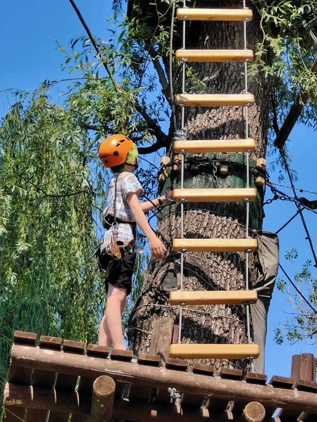 ロープパークの木では 10代の少年が階段をより高く登ろうとしています 下の図 — ストック写真
