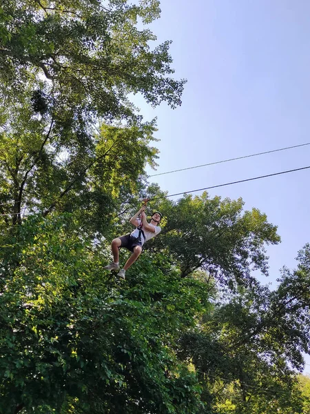 10代の若者が木を背景にロープ遊園地でケーブルカーにロープを降り — ストック写真