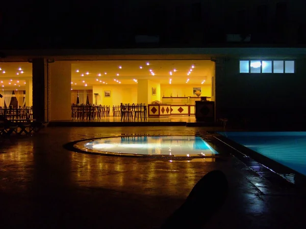 Night hotel without people by the pool and dining room with night lighting