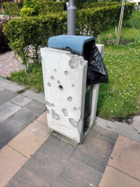 A decorative trash can in a city park with bullet holes as a result of military operations in the Russian-Ukrainian war