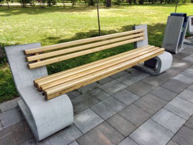 Decorative empty bench made of wood and stone for rest on a street made of concrete slabs in a city park