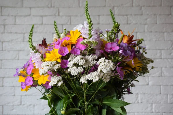 A bouquet of field various fresh flowers in the center of the frame on a blurred background of a light brick wall