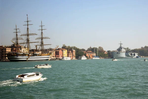 港の反対側の桟橋に立っている古代のマストと近代的な大型軍艦 近くに小さな船が浮かんでいる — ストック写真