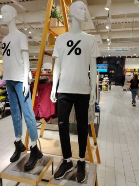 Öndeki giyim mağazasında tişört giyen iki manken var. İndirimli faiz şeklinde bir baskıları var.