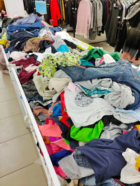 In the second-hand store, there are baskets with a variety of clothes in bulk for different tastes. In the background are racks with hanging clothes