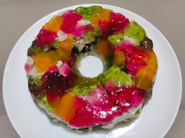 Beyaz seramik bir tabakta farklı parlak renkte bir tatlı jölesi dairesi bulunur.