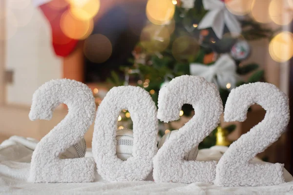 Ett gratulationskort med ett gott nytt år 2022 på bakgrunden av en öppen spis, en julgran, med starkt ljus i en krans. — Stockfoto