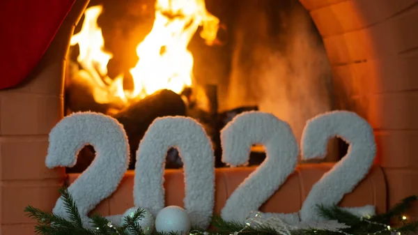 Kartka okolicznościowa ze szczęśliwym nowym rokiem 2022 na tle kominka, choinki, z jasnymi światłami girlandy. Obraz Stockowy
