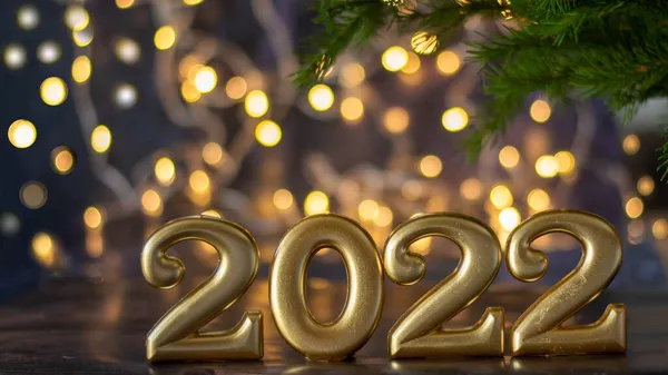 2022年あけましておめでとうございます。金色の数字は、背景にバックライト付きのボケとトウヒの小枝とファッショナブルな青の背景に立っています。. — ストック写真