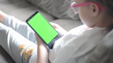 Mutlu küçük bir kız cep telefonunun yeşil ekranına bakar ve komik bir filme güler. Bir cep telefonu monitörünün görüntüsü