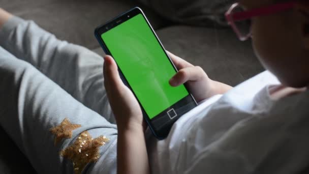 Seorang gadis kecil yang bahagia melihat layar hijau dari telepon genggamnya dan tertawa di film lucu. snapshot dari monitor telepon genggam — Stok Video