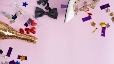 Boş şişeler, bir bardak şarap, kadın ayakkabıları ve pembe bir arka planda papyon olan bir partiyi kutladıktan sonra yukarıdan manzaralı bir resim. Sevgililer Günü 'nü kutluyoruz.