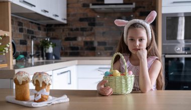 Bandajlı güzel bir çocuk, tavşan kulaklı, renkli yumurtalar sepette, evde, mutfakta. Paskalya için Hazırlık