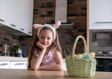Bandajlı güzel bir çocuk, tavşan kulaklı, renkli yumurtalar sepette, evde, mutfakta. Beyaz tüylü bir kedi yakında oturuyor. Paskalya için Hazırlık