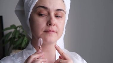 Rahatlamış ve gülümseyen genç bir kadının yakın plan fotoğrafı doğal gül kuvarstan yapılmış bir yüz silindiriyle masaj yaparken..