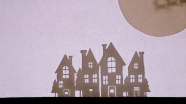 Kukla Gölge Tiyatrosu. Ren geyikleriyle dolu bir kızakta Noel Baba parlayan pencereli evlerin üzerinden dünyaya uçar.