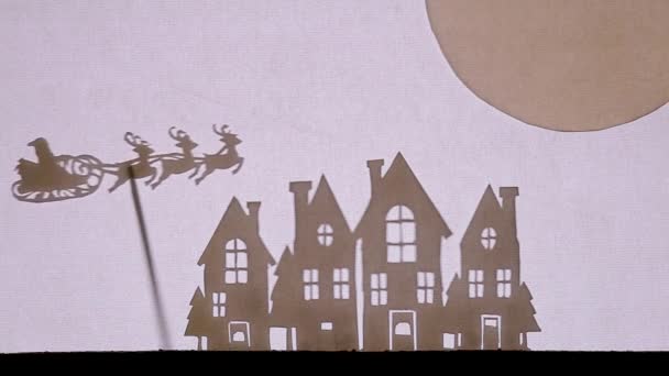 Jultomten flyger över himlen på en släde med ren, stannar sedan vid hustaken i hus med glödande fönster. Sen flyger han till den stora månen — Stockvideo