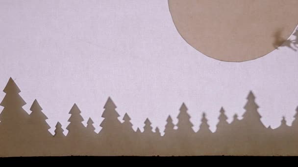 Teatro das Sombras de Marionetas. Papai Noel em um trenó com renas voando sobre a floresta com a lua grande no canto direito — Vídeo de Stock