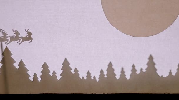 Bábszínház Árnyék Színház. Mikulás egy szánon rénszarvas repül az erdő felett a nagy hold alatt a jobb sarokban — Stock videók
