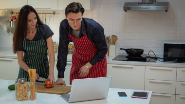 Beyaz Kafkasyalı çiftler ya da aşıklar modern mutfakta dizüstü bilgisayarla ya da defterle yemek yapmayı öğreniyorlar..